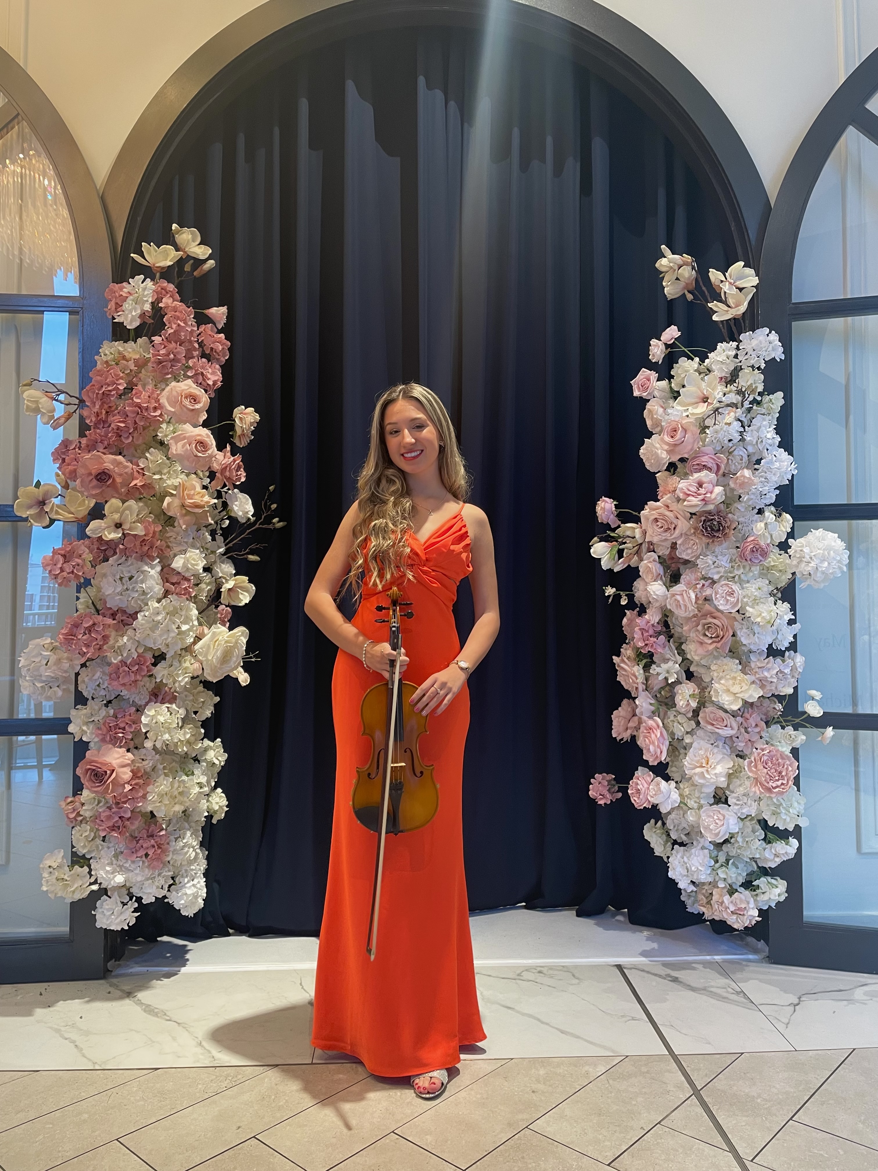 Tali in orange dress standing in front of flower arrangement